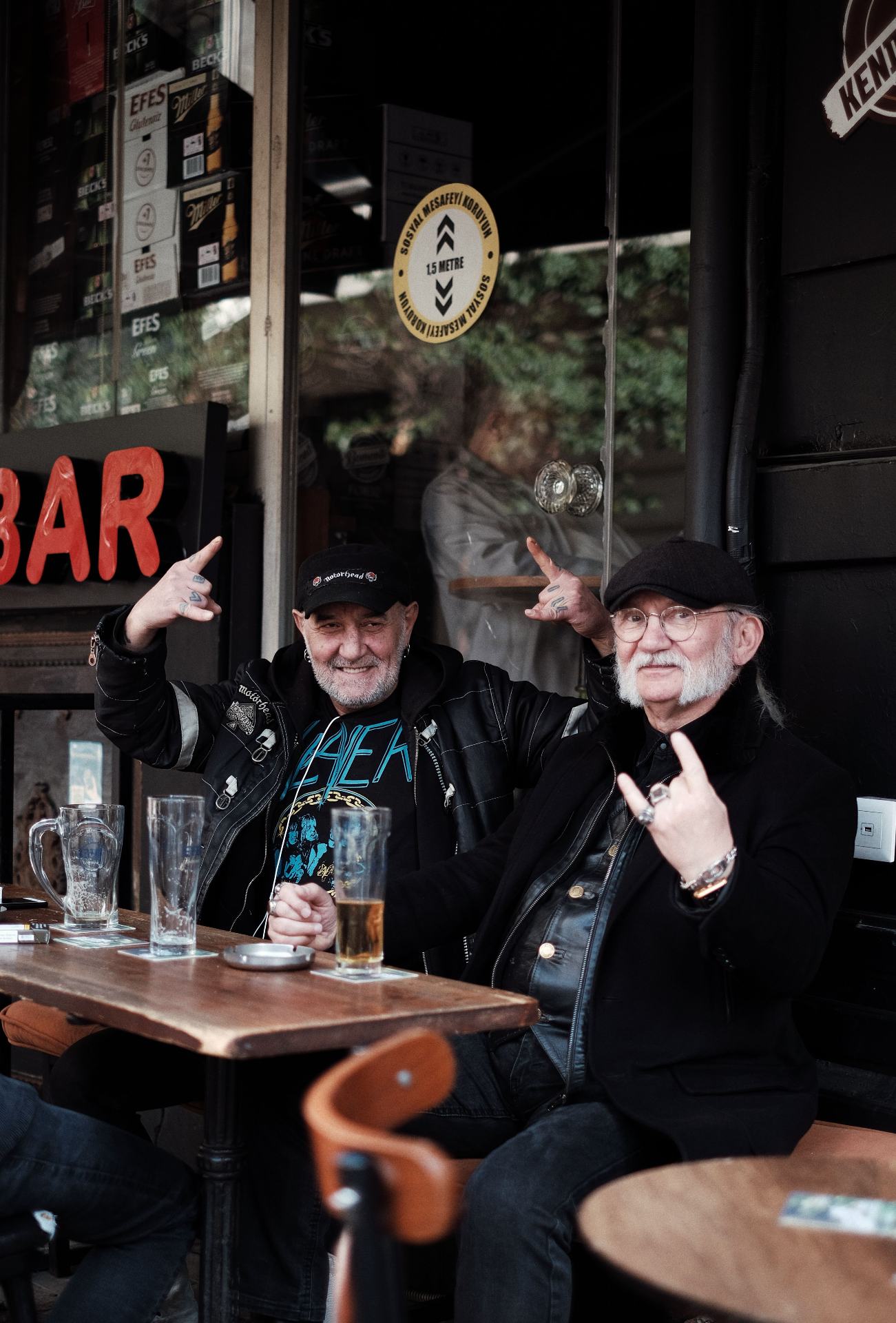 Two mates throwing rock horns with beers at a bar